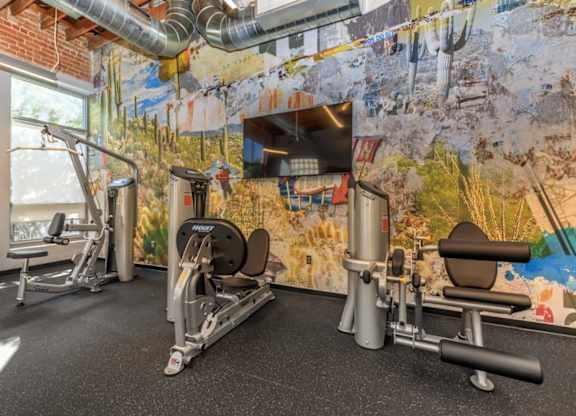 A gym with a wall mural and a row of exercise machines.