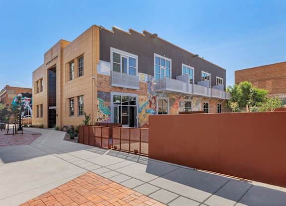A building with a mural on the side has a red fence in front of it.