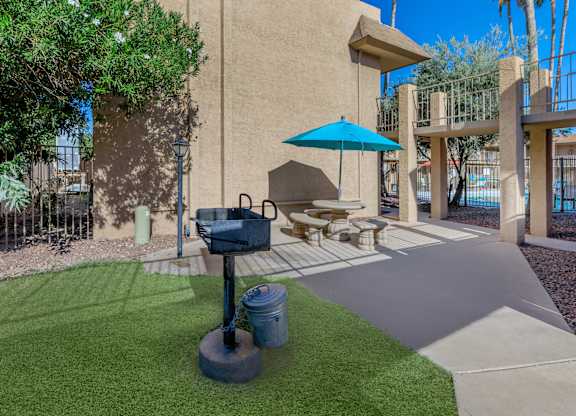 A patio with a blue umbrella and a grill.