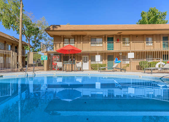 A swimming pool in front of a building with a red umbrella.