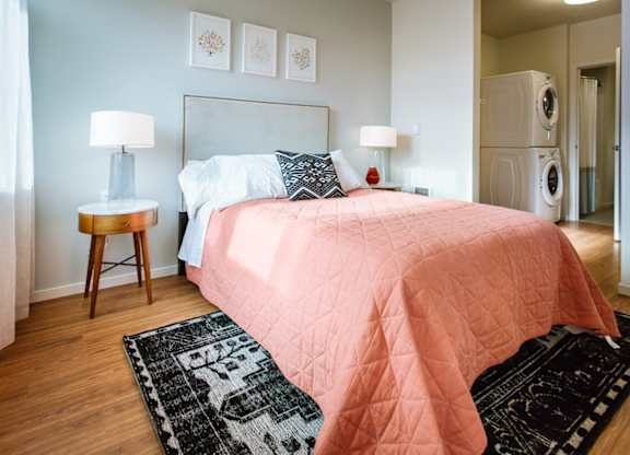 A bedroom with a pink bedspread and a black and white rug.