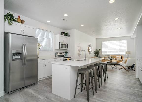 a white kitchen with stainless steel appliances and bar stools
