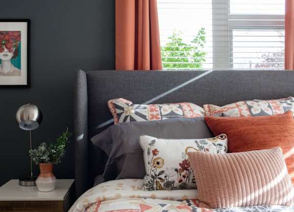 A bed with a grey headboard and a white pillow with a floral pattern.