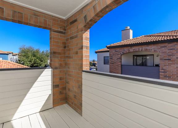 A balcony with a white railing and a brick chimney on a house.