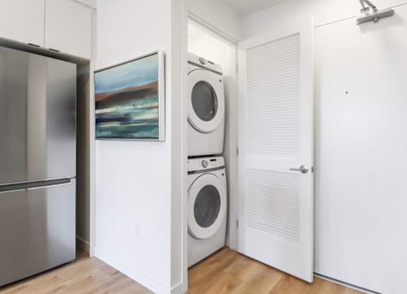 A white laundry room with a refrigerator, a washer and a dryer.