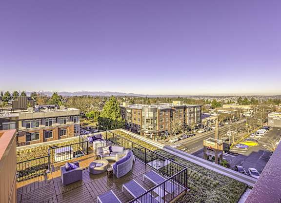 A rooftop patio with a table and chairs overlooks a cityscape.