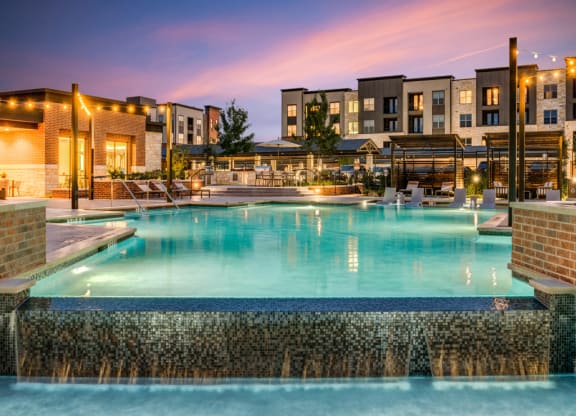 a swimming pool at night with apartments in the background