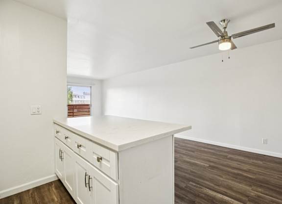 A white kitchen with a ceiling fan and wooden flooring.
