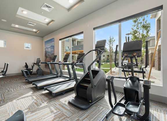 a gym with cardio equipment and large windows