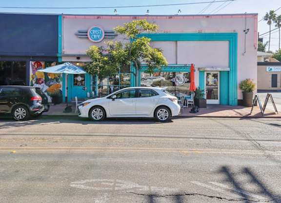 A white car is parked in front of a pink building with a blue door.