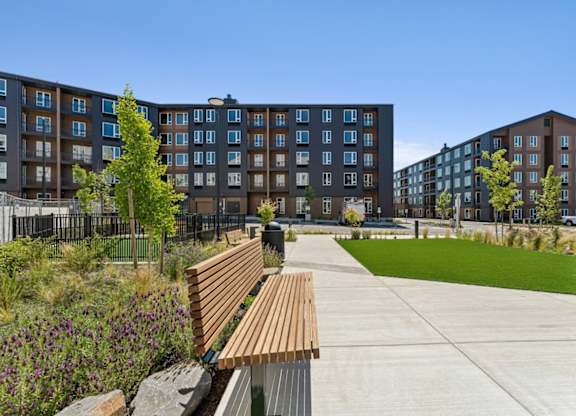 A wooden bench sits on a concrete path in front of apartment buildings.