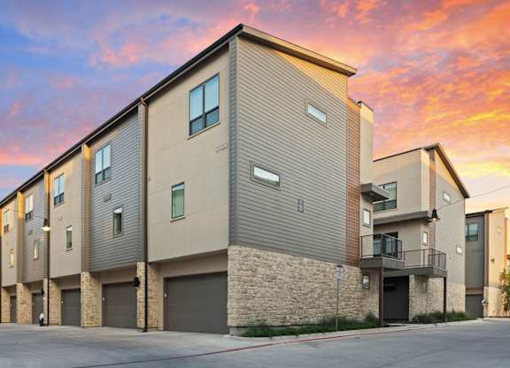 A modern apartment building with a sunset sky in the background.