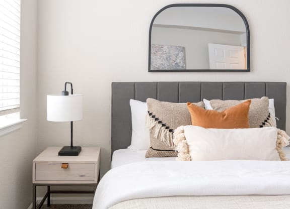 a bedroom with a bed and a nightstand with a lamp and a mirror above it