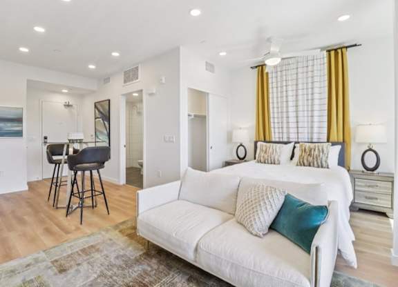 A white couch with blue and white pillows sits in a living room with a bar area and a dining area in the background.