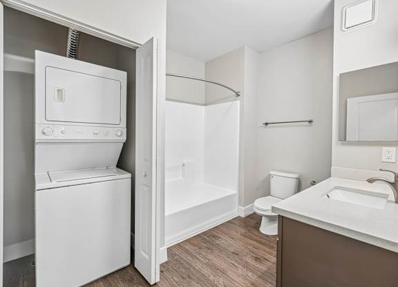 A white washing machine is in a small bathroom with a toilet and sink.