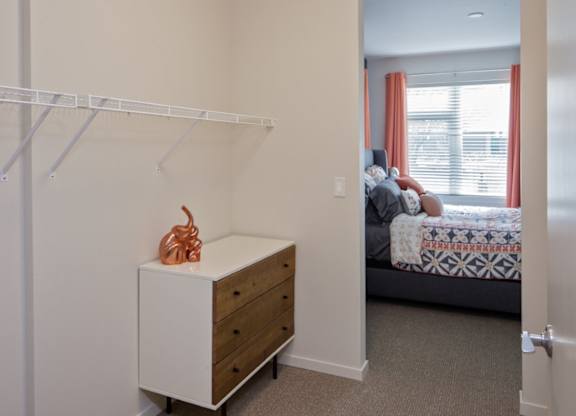 A white cabinet with a brown sculpture on top is in a room with a bed in the background.