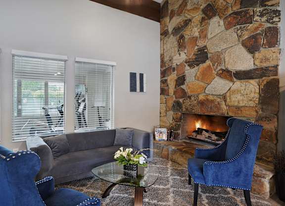 A living room with a stone fireplace and blue chairs.