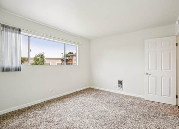 A room with a white door and a window with a view of buildings outside.