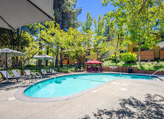 A small pool surrounded by trees and a red pavilion.