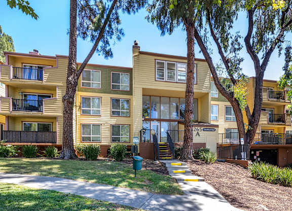 A yellow apartment building with a green trash can in front.
