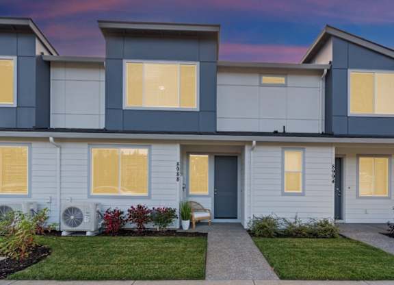 A modern two-story house with a front yard and a pathway leading to the entrance.