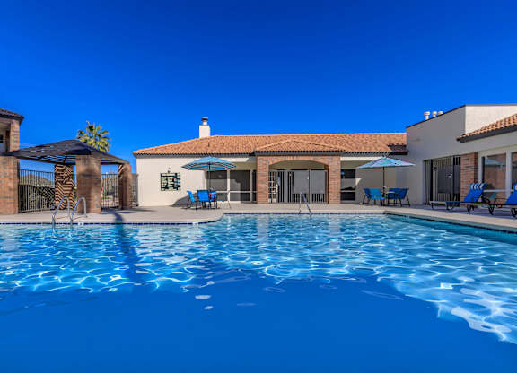 A swimming pool in front of a house with a blue sky.