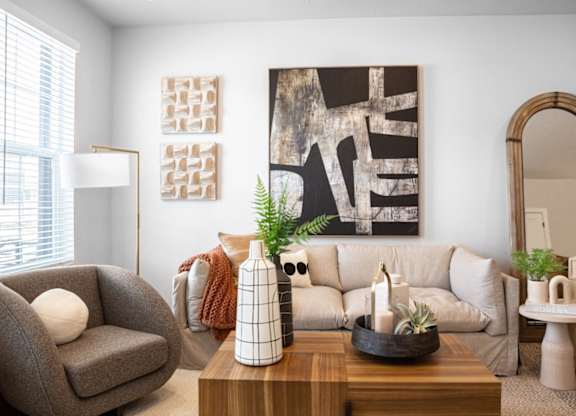 A living room with a grey armchair, a wooden coffee table, and a large abstract painting on the wall.