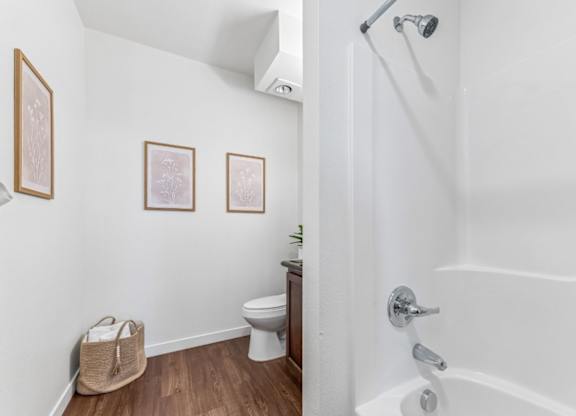 A white bathroom with a toilet, a plant, and pictures on the wall.