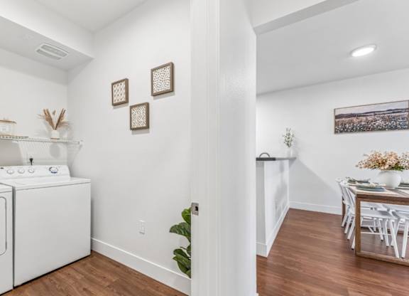 A laundry room with a washer and dryer, a dining table with chairs, and a potted plant.
