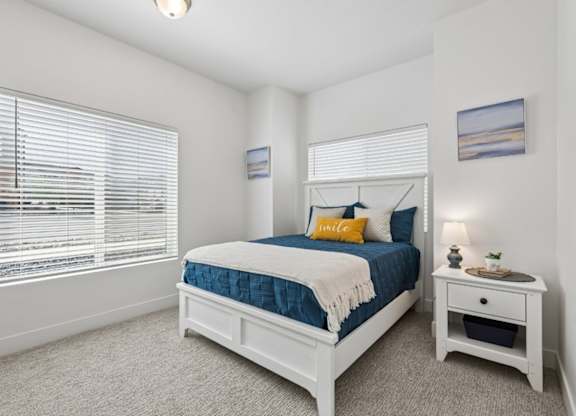 A bedroom with a bed, nightstand, and window with blinds.
