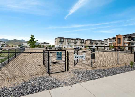 A fenced area with a sign that reads "Bark Park" in front of apartment buildings.