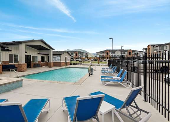 A pool surrounded by blue lounge chairs and a black fence.