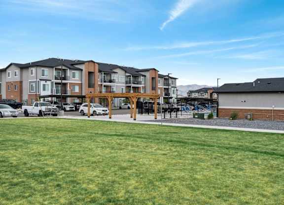 A large grassy area in front of apartment buildings with cars parked in the background.