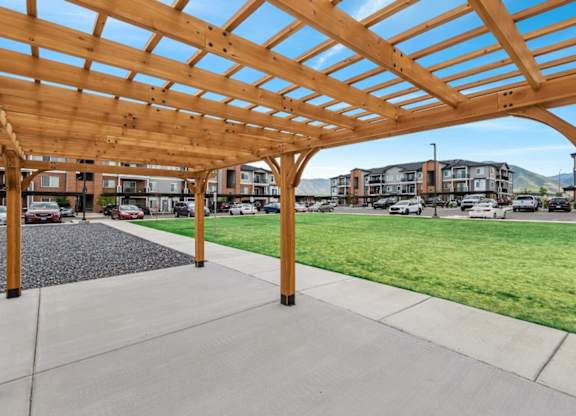 A wooden pergola structure with a concrete floor and grassy area in the background.