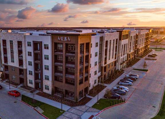 A sunset view of a street with cars and apartment buildings.