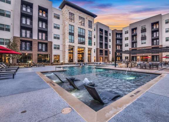 A large outdoor pool surrounded by buildings with a sunset in the background.