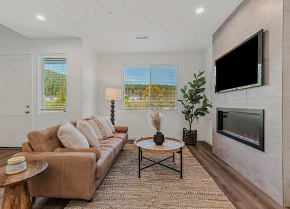 A living room with a brown couch, a coffee table, and a flat screen TV mounted on the wall.