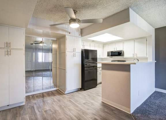 A kitchen with a black fridge and microwave, white cabinets, and a wooden floor.