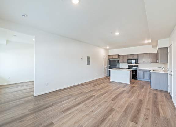 A spacious room with wooden flooring and a kitchen area in the background.