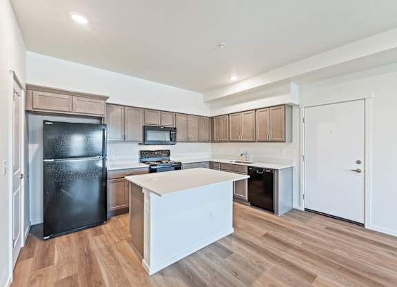 A kitchen with a black fridge and wooden floors.