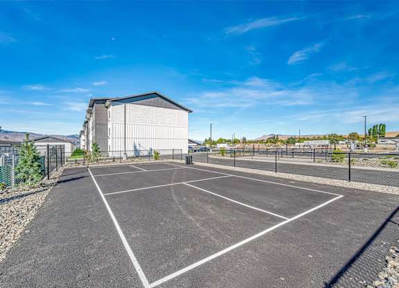 A tennis court is surrounded by a fence and a building.