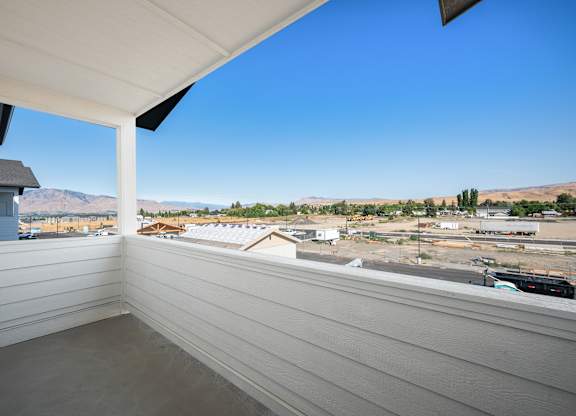 A balcony with a view of a construction site and distant houses.
