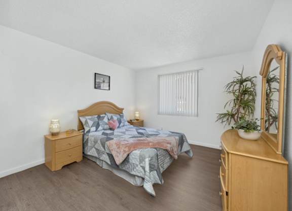 A bedroom with a bed, nightstand, and a plant.