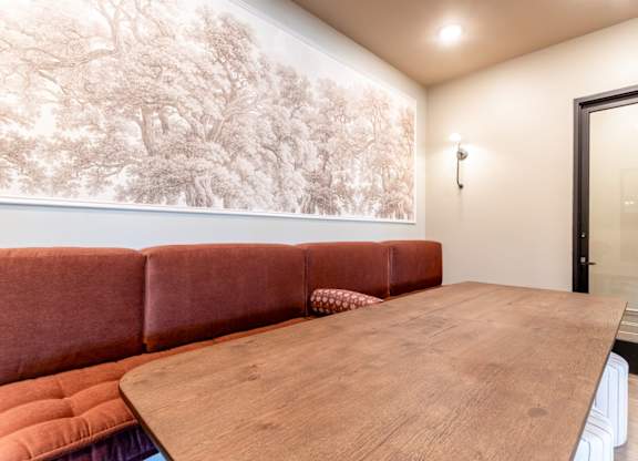 A brown leather couch sits in front of a large wall mural in a room with a wooden table.