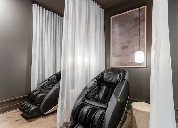 Two black massage chairs with white curtains on the side.