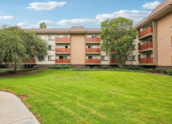 A grassy area in front of a building with trees and bushes.
