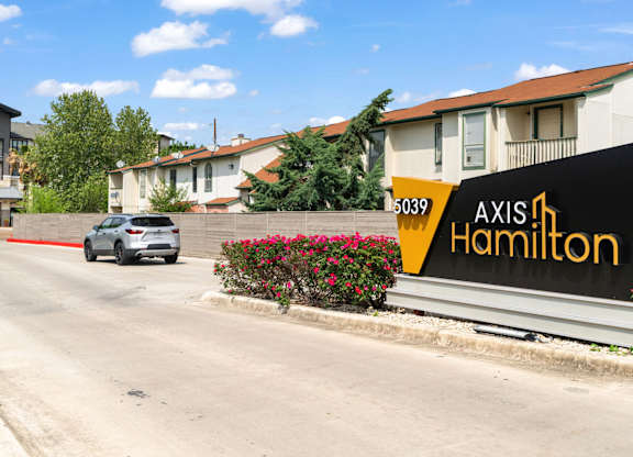 A white car is driving down a street past a building with a sign that says "Axis Hamilton.".