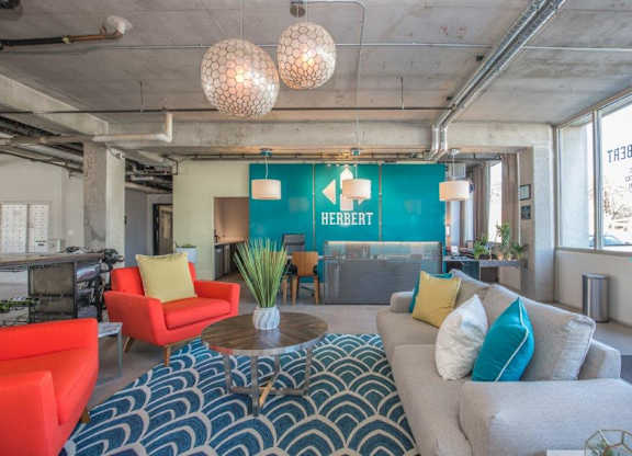 A living room with a blue and white patterned rug, a grey couch, a red chair, and a wooden coffee table at Herbert Residential, Tucson, Arizona