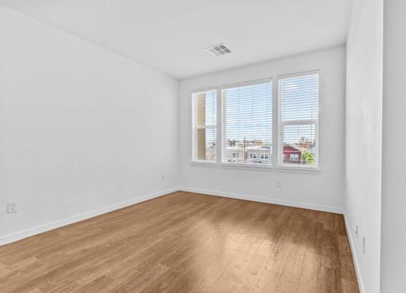 A room with wooden flooring and a window showing a view of a house.