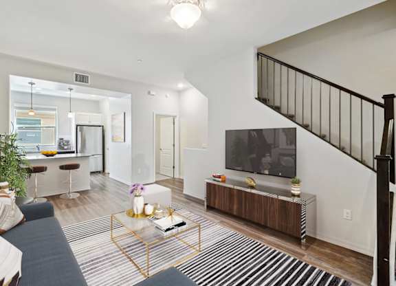 A living room with a black and white striped rug, a wooden coffee table, a TV, and a staircase with a black railing.